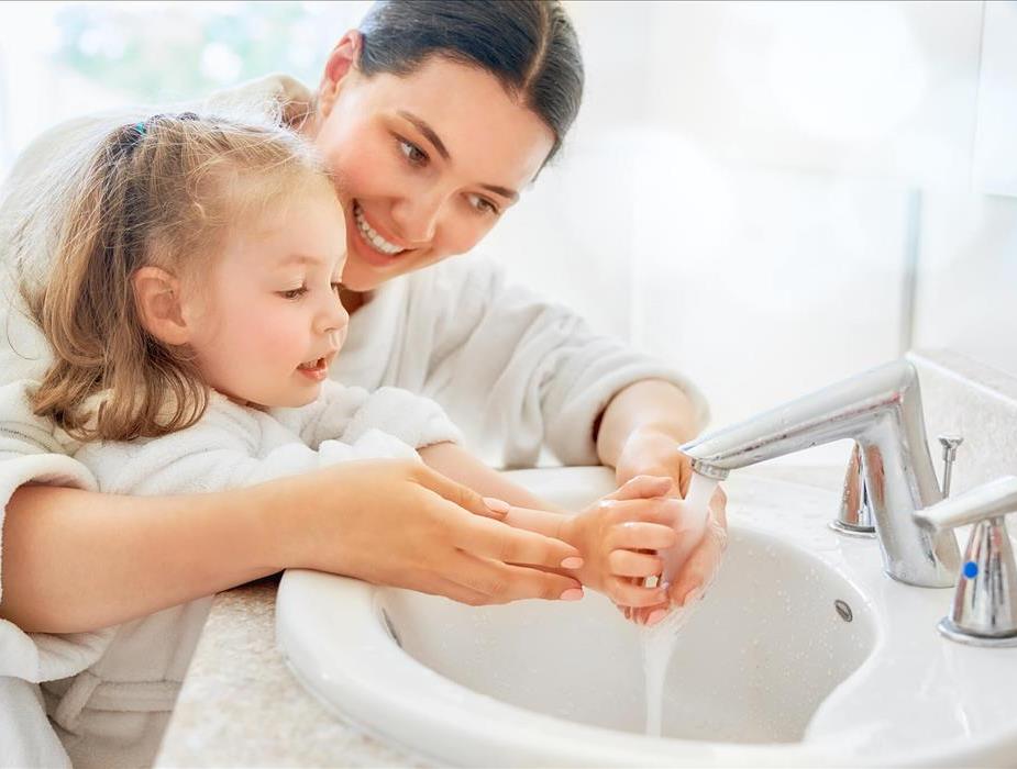 A mother helps her daughter wash her hands